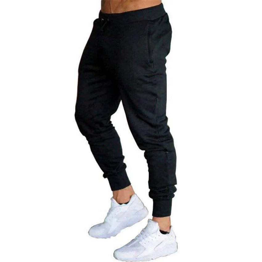 Man wearing black slim-fit jogger pants and white athletic sneakers standing on white background