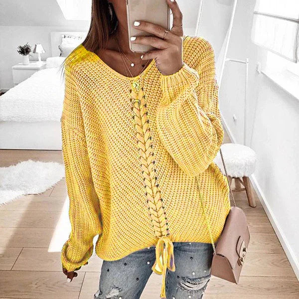 Woman in yellow chunky knit sweater with lace-up front detail and distressed jeans in bright room
