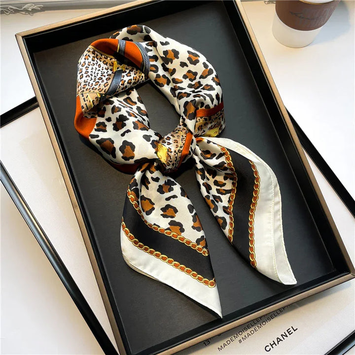 Elegant leopard print silk scarf with chain border design displayed in black tray on white surface