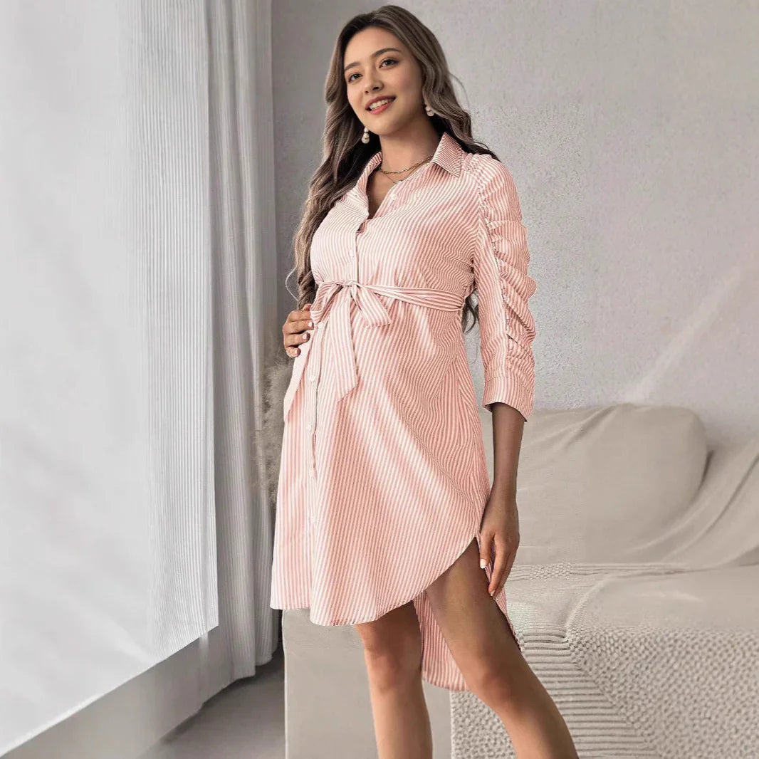 Smiling pregnant woman in pink striped maternity dress with front buttons, standing indoors