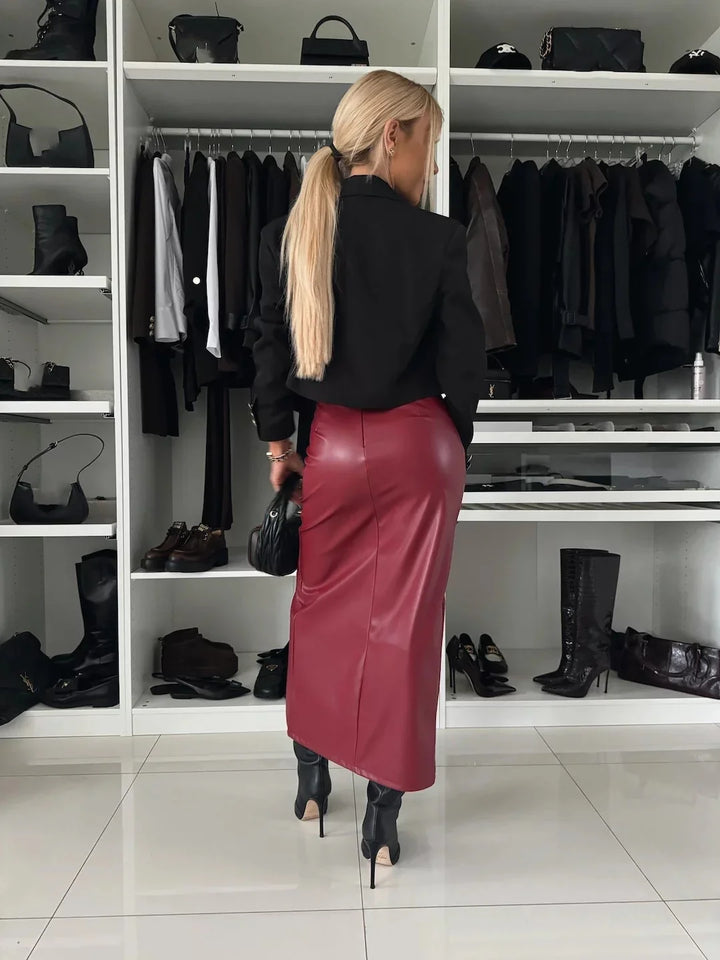 Woman in black top and red leather skirt holding black bag in modern closet with shoes and handbags