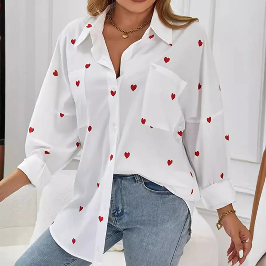 White button-up shirt with red heart print worn with blue jeans, featuring rolled sleeves and gold jewelry