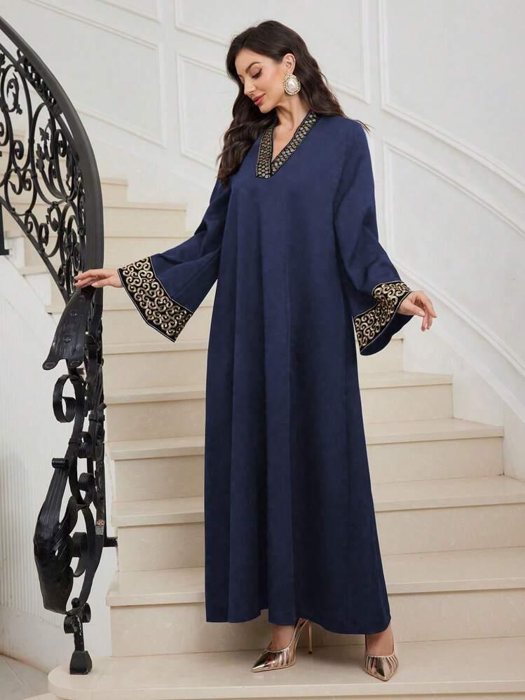 Woman wearing navy blue maxi abaya with gold embroidered trim on sleeves and neckline, standing on white stairs