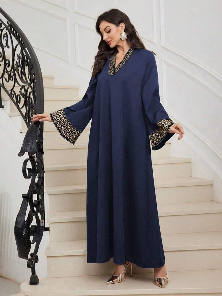 Woman wearing navy blue maxi abaya with gold embroidered trim on sleeves and neckline, standing on white stairs