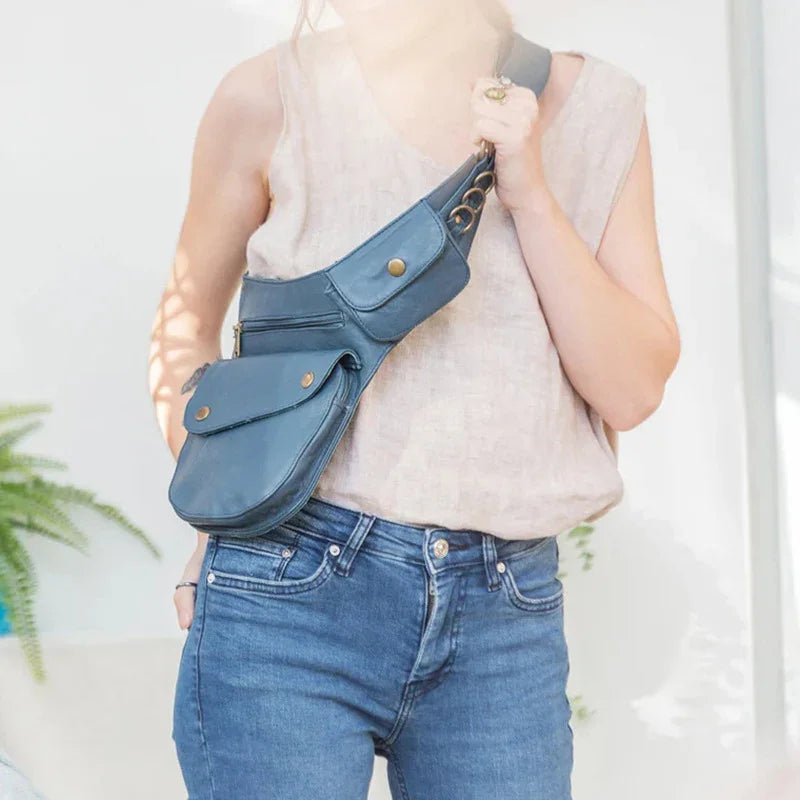 Person wearing sleeveless beige top and blue jeans with blue leather crossbody bag with multiple pockets