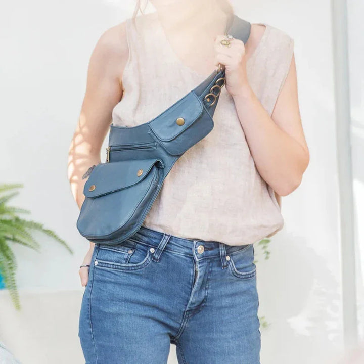 Person wearing sleeveless beige top and blue jeans with blue leather crossbody bag with multiple pockets