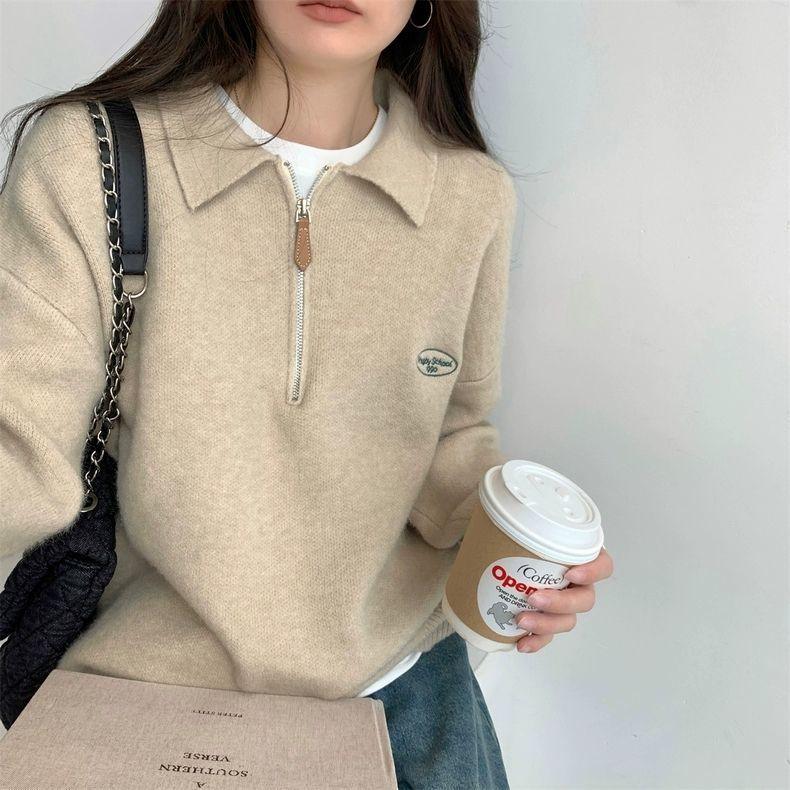Woman in beige zip-up sweater holding coffee cup with black chain strap bag and book