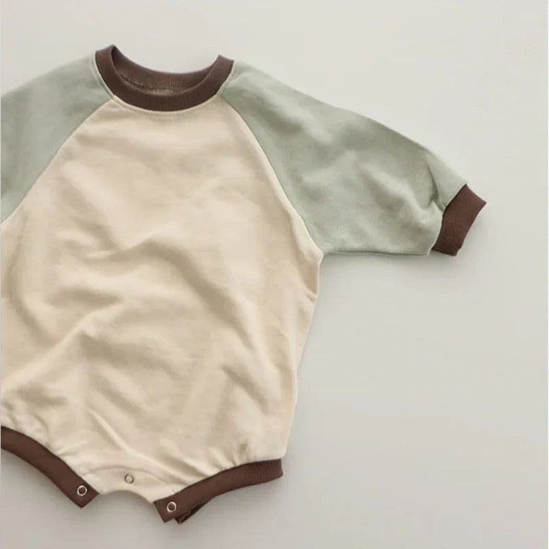 Beige and light green baby romper with brown trim and snap closures on a white background