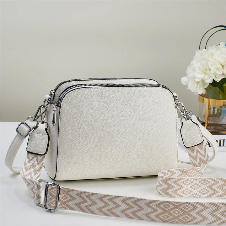 White textured crossbody bag with dual zip compartments and patterned beige adjustable strap
