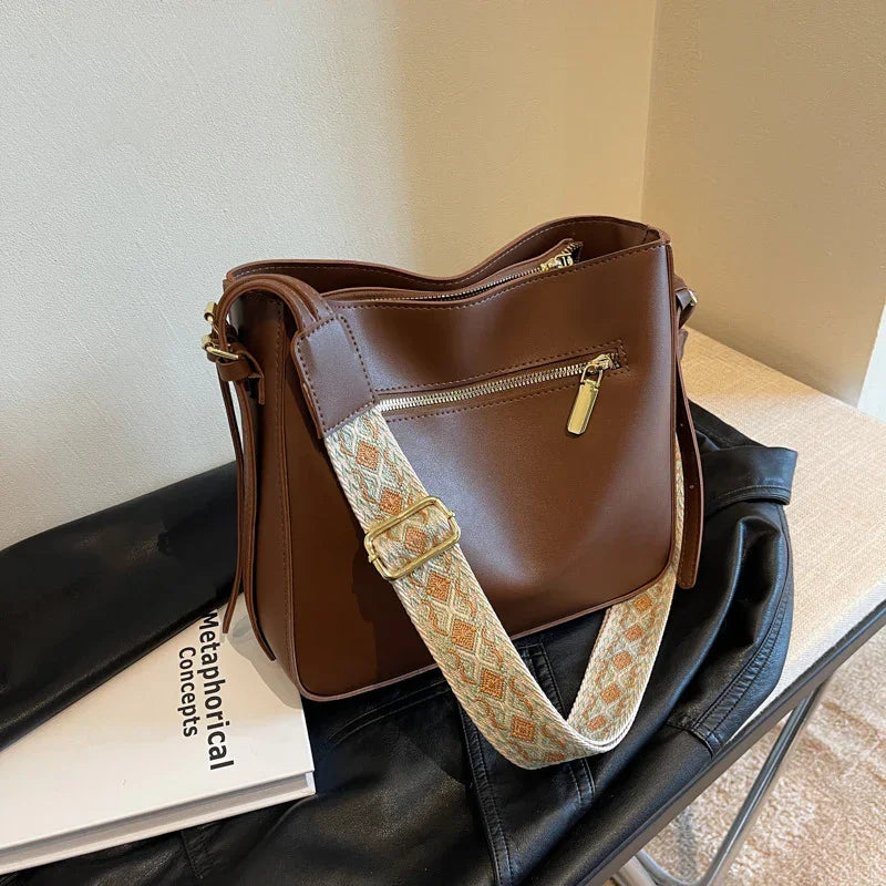 Brown leather crossbody bag with patterned adjustable strap on black leather jacket and book