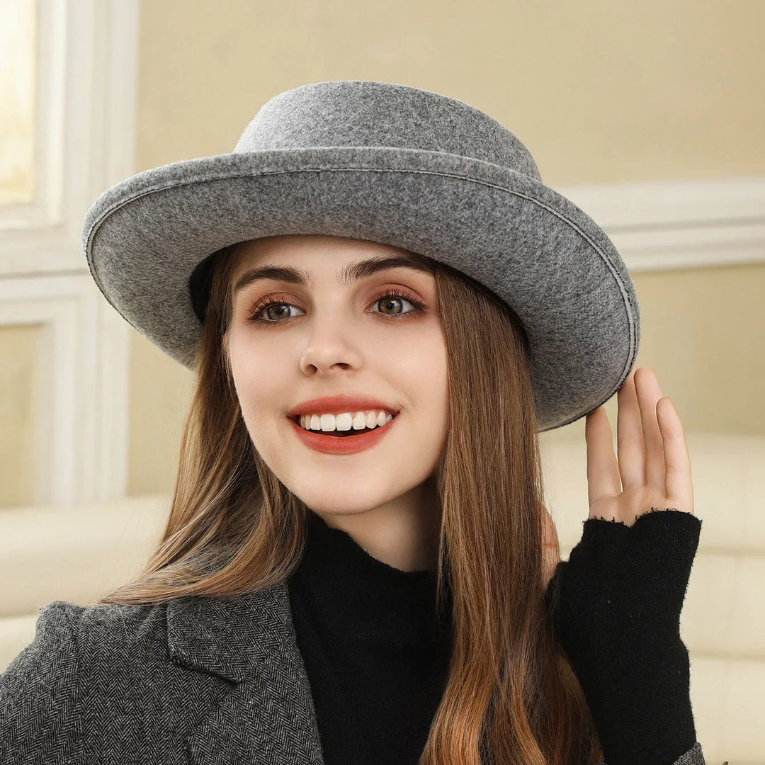 Smiling woman wearing a gray wool hat and matching blazer with black turtleneck indoors