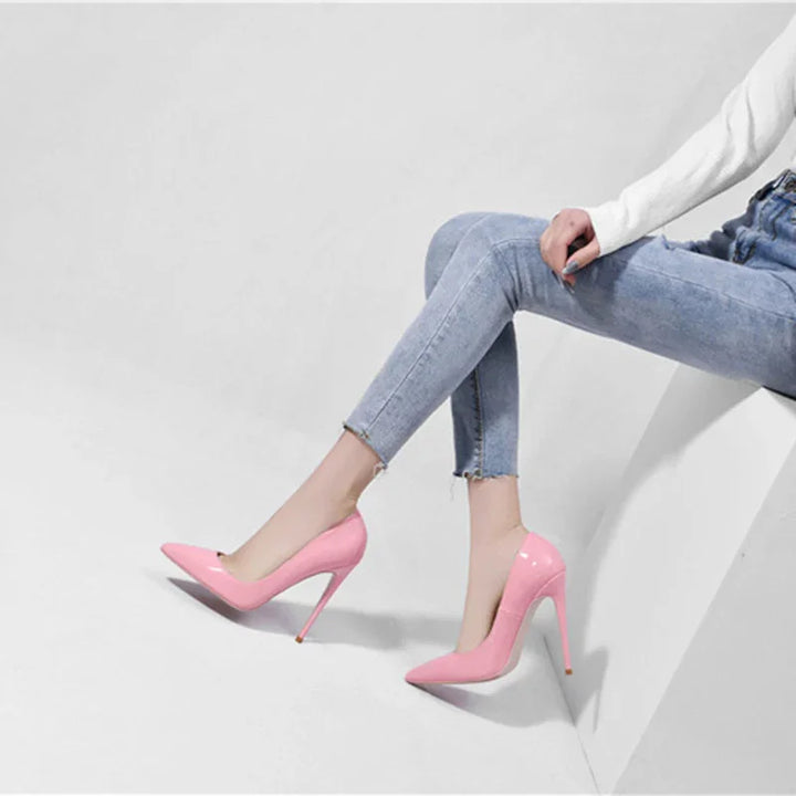 Woman wearing light blue skinny jeans and glossy pink high heel shoes sitting on white surface