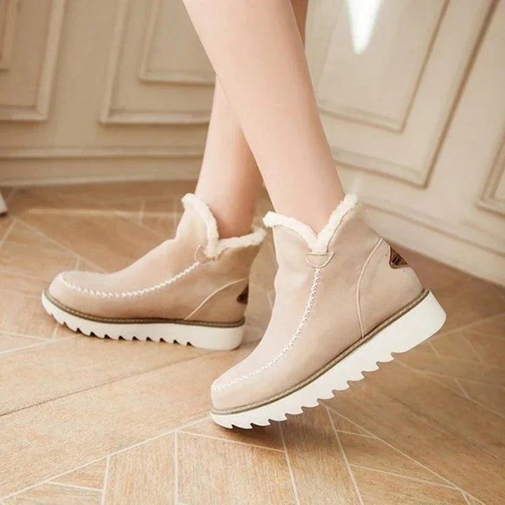 Beige winter ankle boots with white fur lining and thick white ridged soles on tiled floor