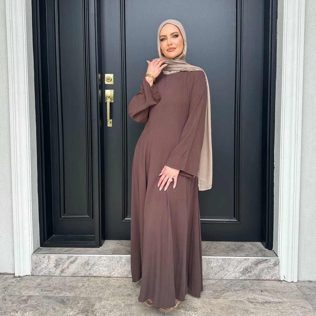 Woman wearing brown long abaya dress and beige hijab standing by black front door with gold handle