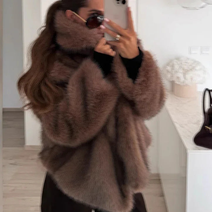 Woman wearing oversized brown fur coat and sunglasses taking mirror selfie indoors