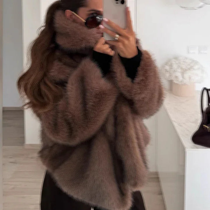 Woman wearing oversized brown fur coat and sunglasses taking mirror selfie indoors