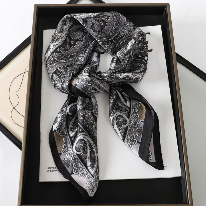 Black and gray paisley silk scarf with intricate patterns, displayed in a framed box with artwork underneath