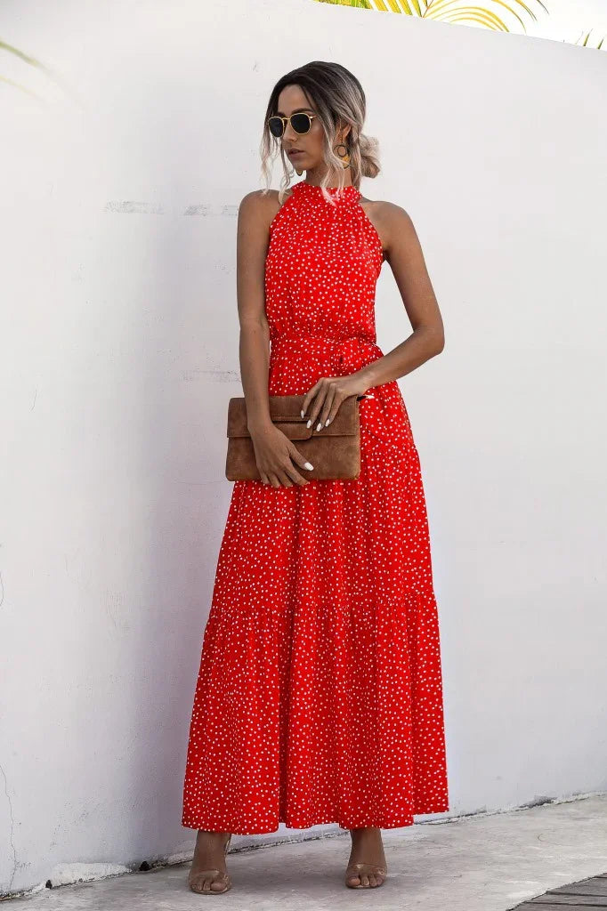 Woman wearing a red polka dot halter maxi dress with sunglasses and holding a brown clutch