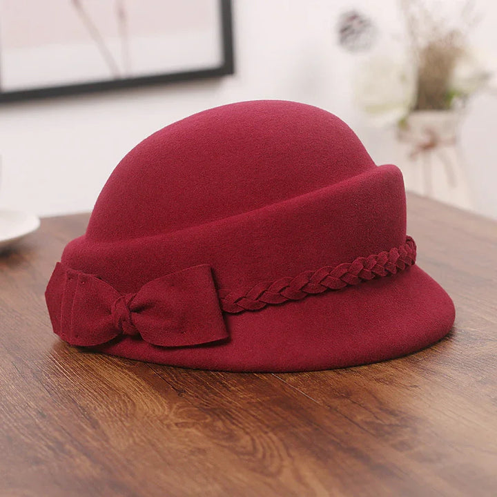 Elegant deep red felt cloche hat with braided band and bow on wooden surface