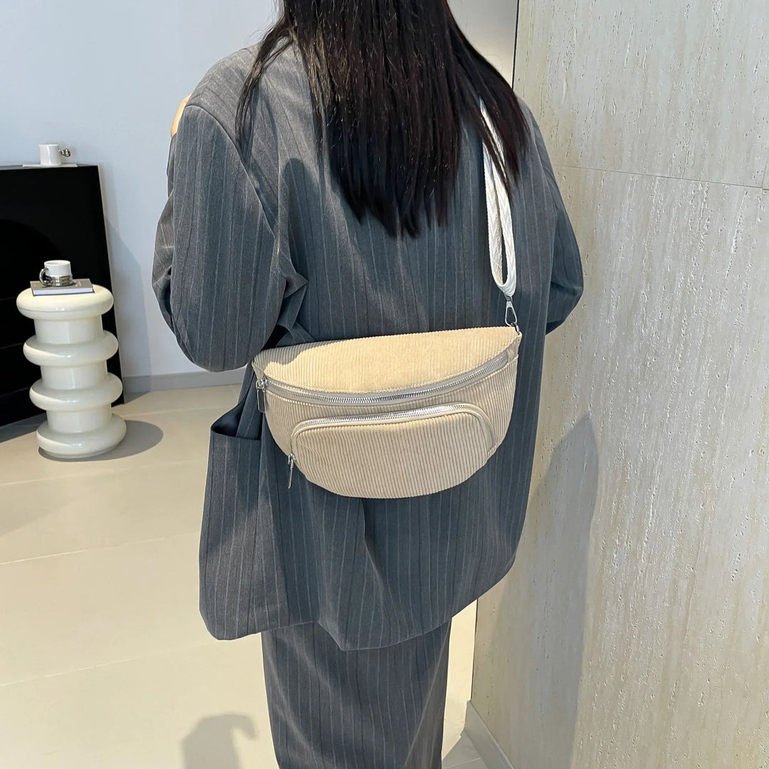 Woman wearing gray pinstripe suit with beige corduroy crossbody bag in modern minimalist room