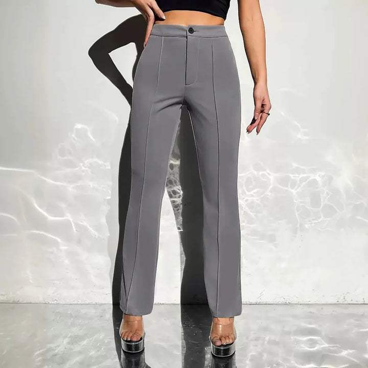 Woman wearing high-waisted gray tailored pants and clear platform heels against white wall