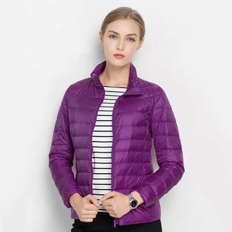 Woman wearing a purple lightweight quilted jacket over a black and white striped shirt with a neutral background