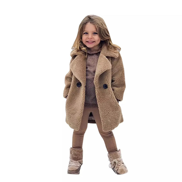 Smiling young girl wearing a beige teddy coat, brown sweater, leggings, and fur-lined winter boots