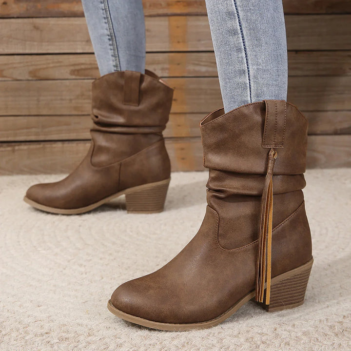 Women's brown slouchy ankle boots with tassel detail and block heel, styled with light denim jeans