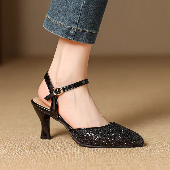 Black glitter pointed toe slingback heel with ankle strap on foot and blue denim jeans