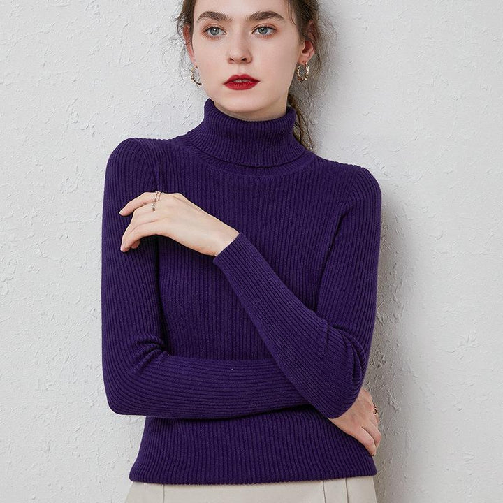 Woman wearing a purple ribbed turtleneck sweater posing against a textured light gray wall