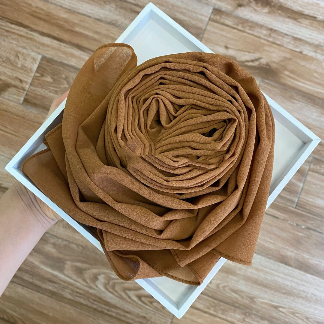 Hand holding white box with neatly rolled soft brown fabric or scarf on wooden floor