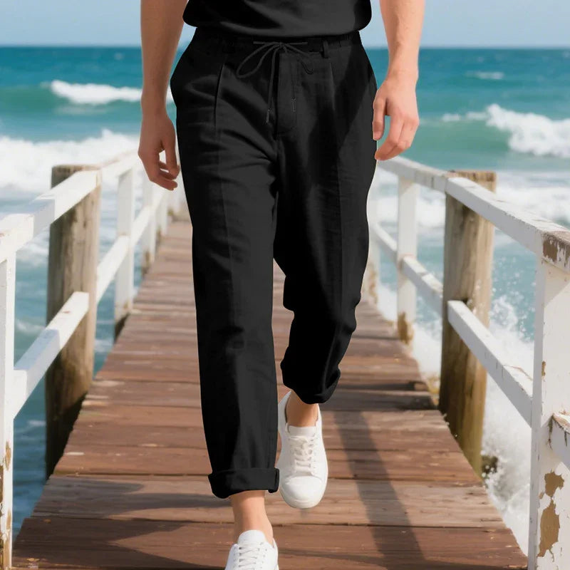 Man wearing black casual pants and white sneakers walking on wooden pier by ocean