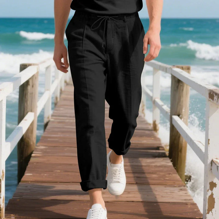 Man wearing black casual pants and white sneakers walking on wooden pier by ocean