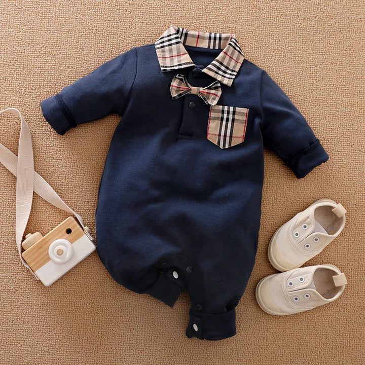 Navy blue baby romper with plaid collar, bow tie, pocket, paired with beige baby shoes and wooden toy camera