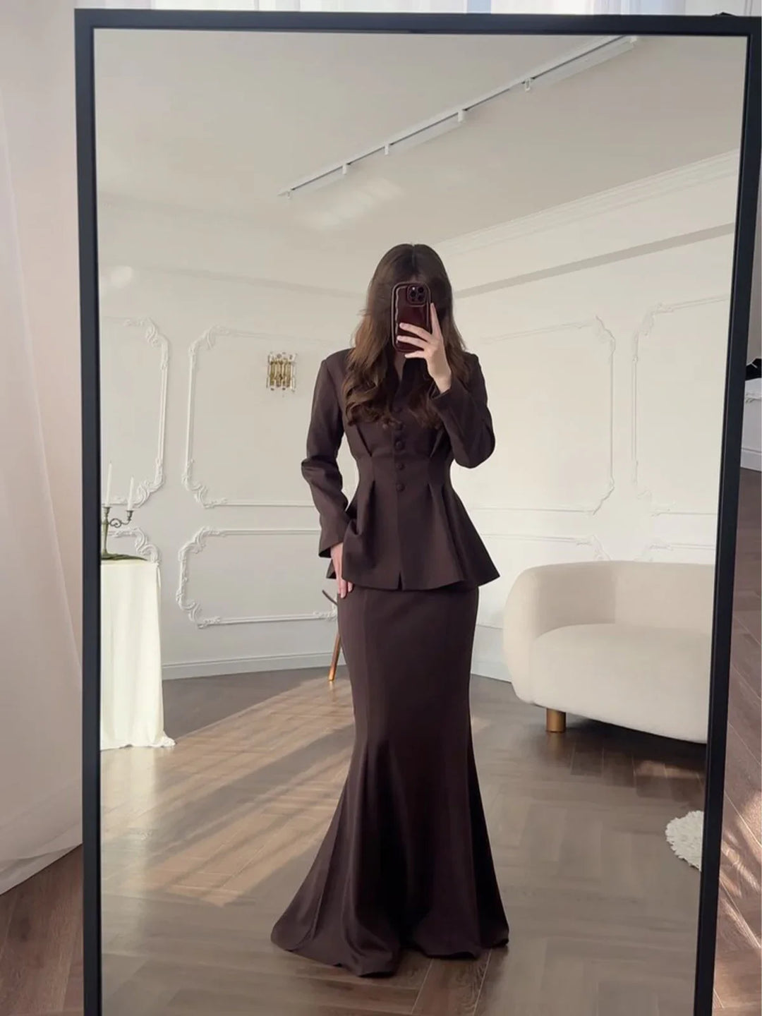 Woman taking mirror selfie wearing elegant dark brown peplum blazer and long fitted skirt in stylish room