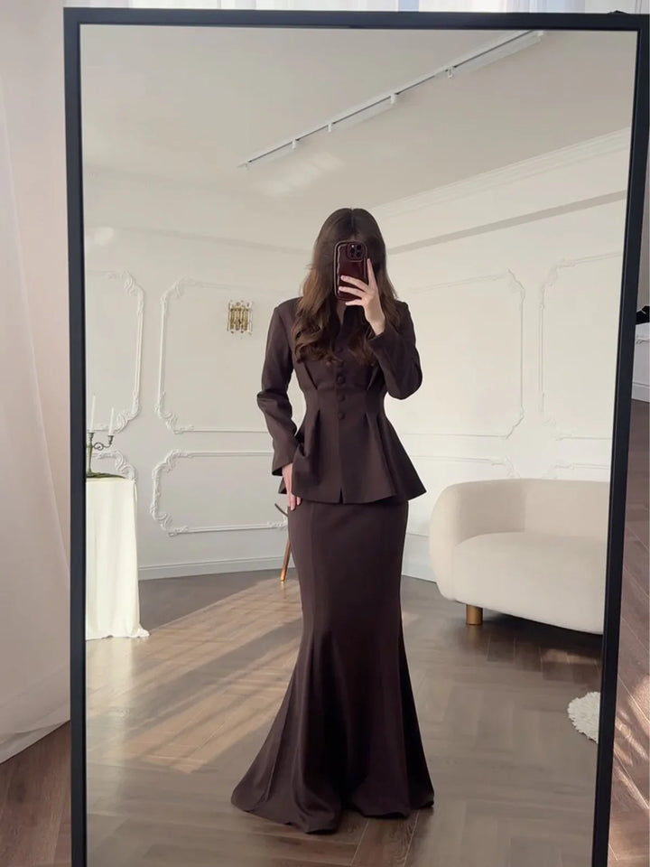 Woman taking mirror selfie wearing elegant dark brown peplum blazer and long fitted skirt in stylish room