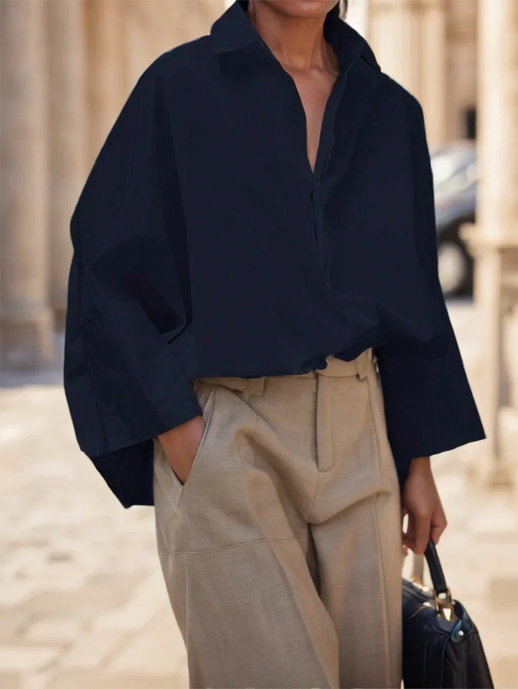 Person wearing a loose black blouse with wide sleeves and beige high-waisted pants holding a navy handbag