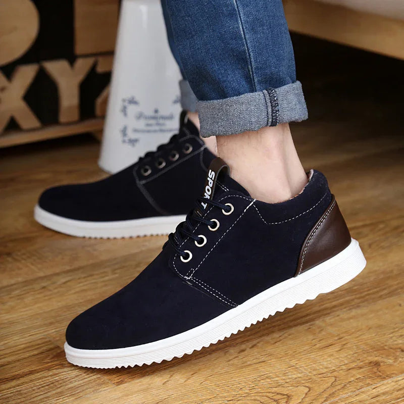 Black casual sneakers with white sole and brown heel detail worn with rolled-up blue jeans on wooden floor