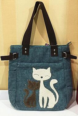 Blue tote bag with black handles featuring white and brown cat design on front pocket