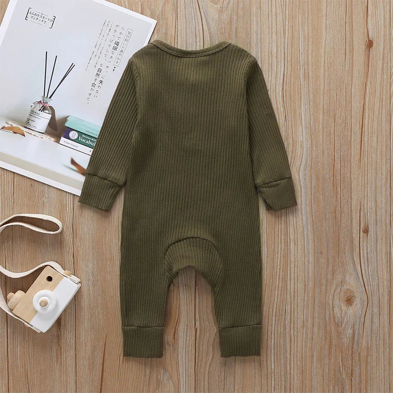 Olive green ribbed knit baby romper on wooden surface with toy camera and book