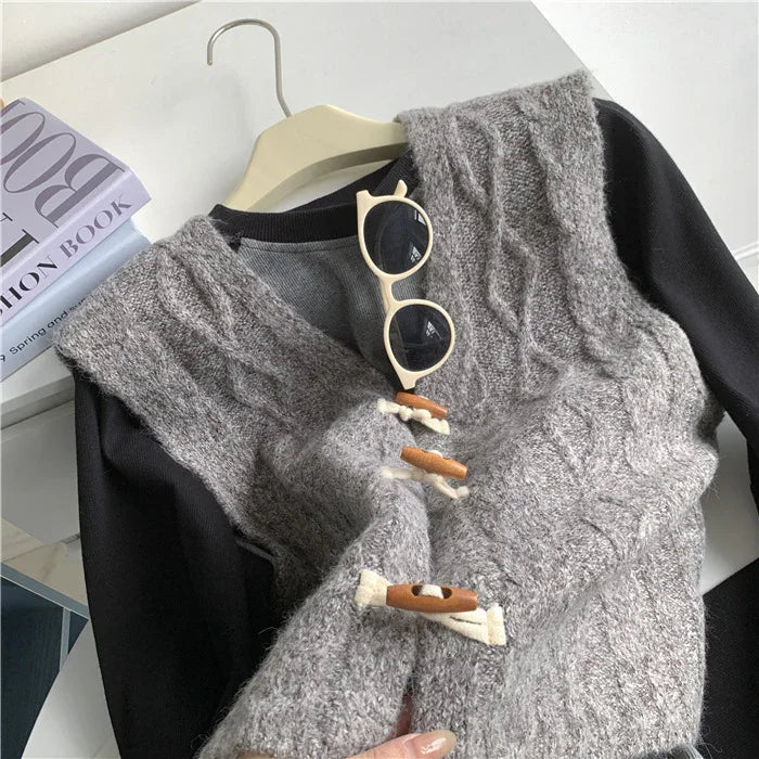 Grey cable knit wool vest with wooden toggle buttons layered over black long sleeve shirt, beige sunglasses on hanger