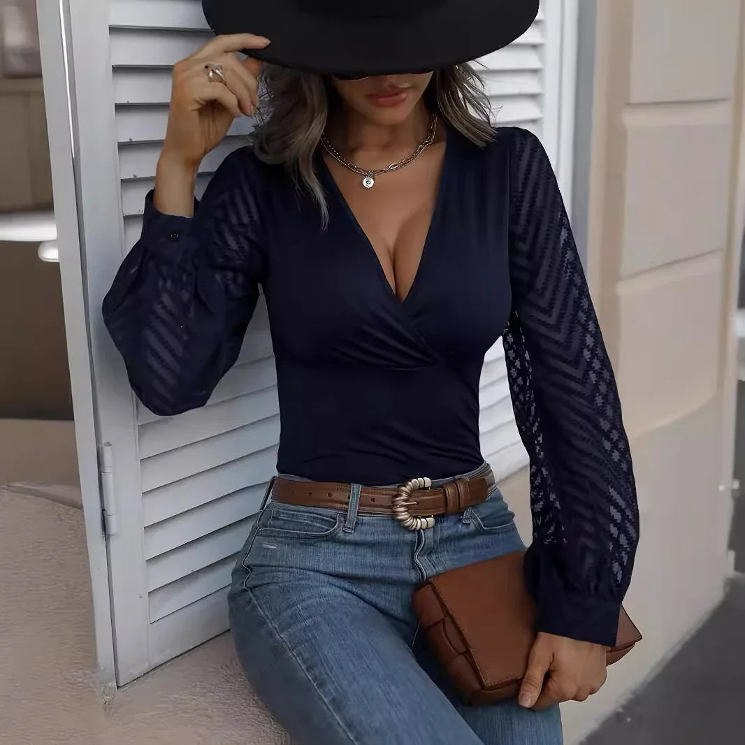 Woman in navy blue lace sleeve top, jeans, brown belt, and hat holding a brown clutch
