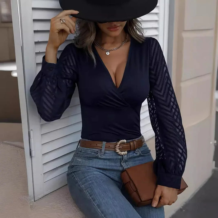 Woman in navy blue lace sleeve top, jeans, brown belt, and hat holding a brown clutch