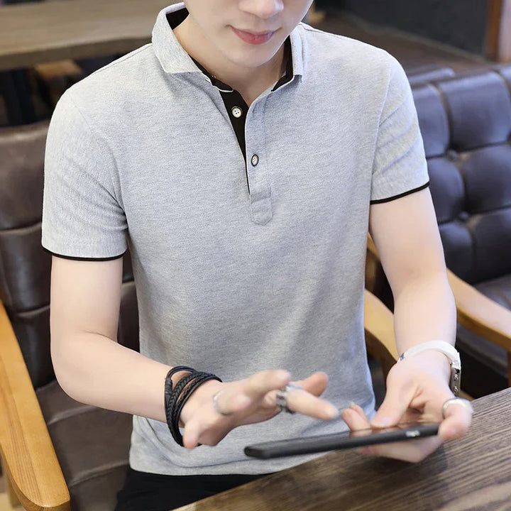 Man wearing grey polo shirt with black trim using smartphone seated on brown chair