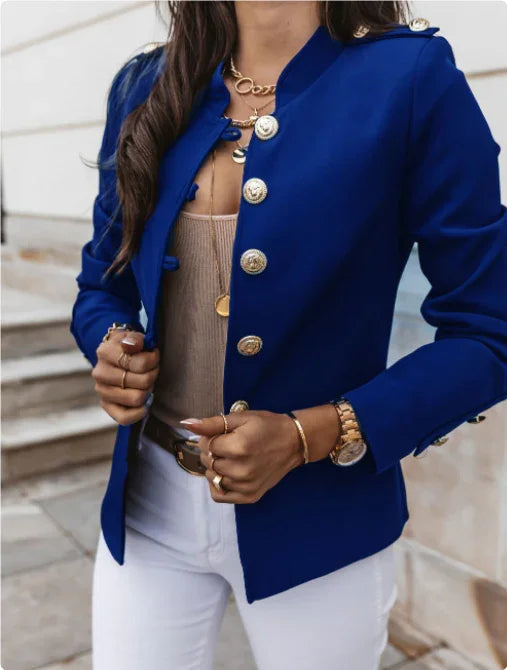 Woman wearing stylish royal blue blazer with gold buttons, layered gold necklaces, white pants, and gold watch