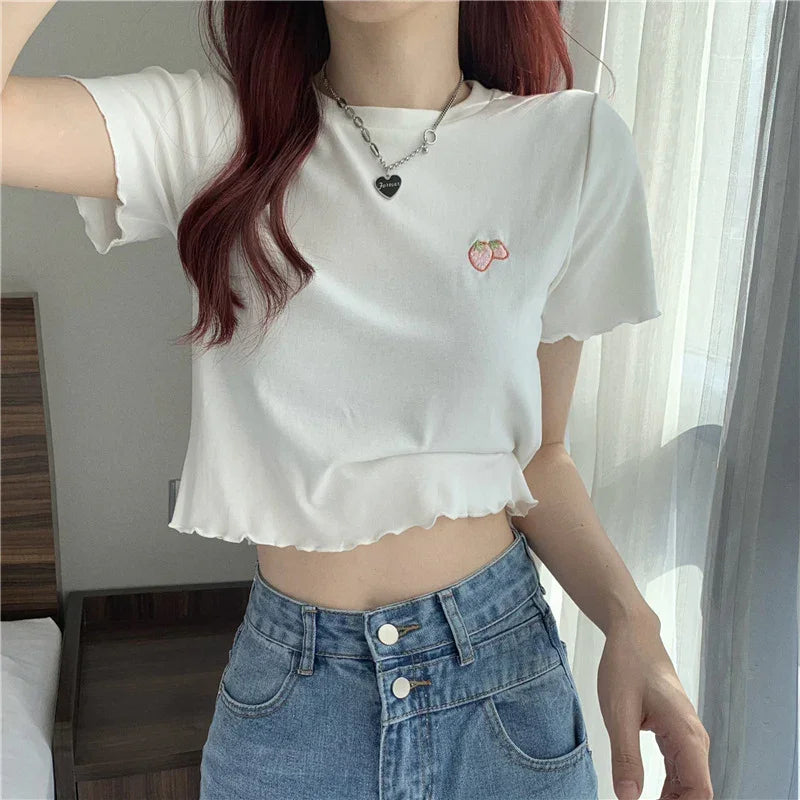 Woman wearing a white cropped t-shirt with strawberry embroidery and high-waisted blue jeans