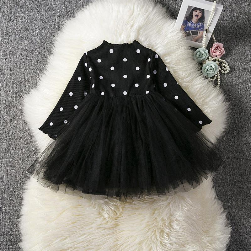 Black long-sleeve toddler dress with white polka dots and layered tulle skirt on white fur rug