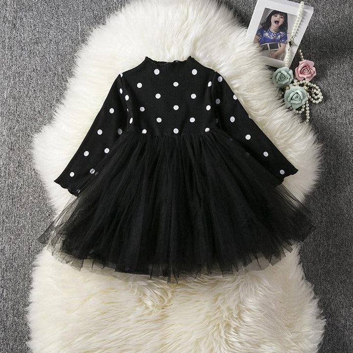 Black long-sleeve toddler dress with white polka dots and layered tulle skirt on white fur rug