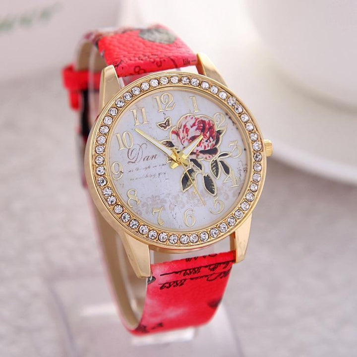 Gold wristwatch with rhinestone bezel, floral dial design, and red patterned leather strap