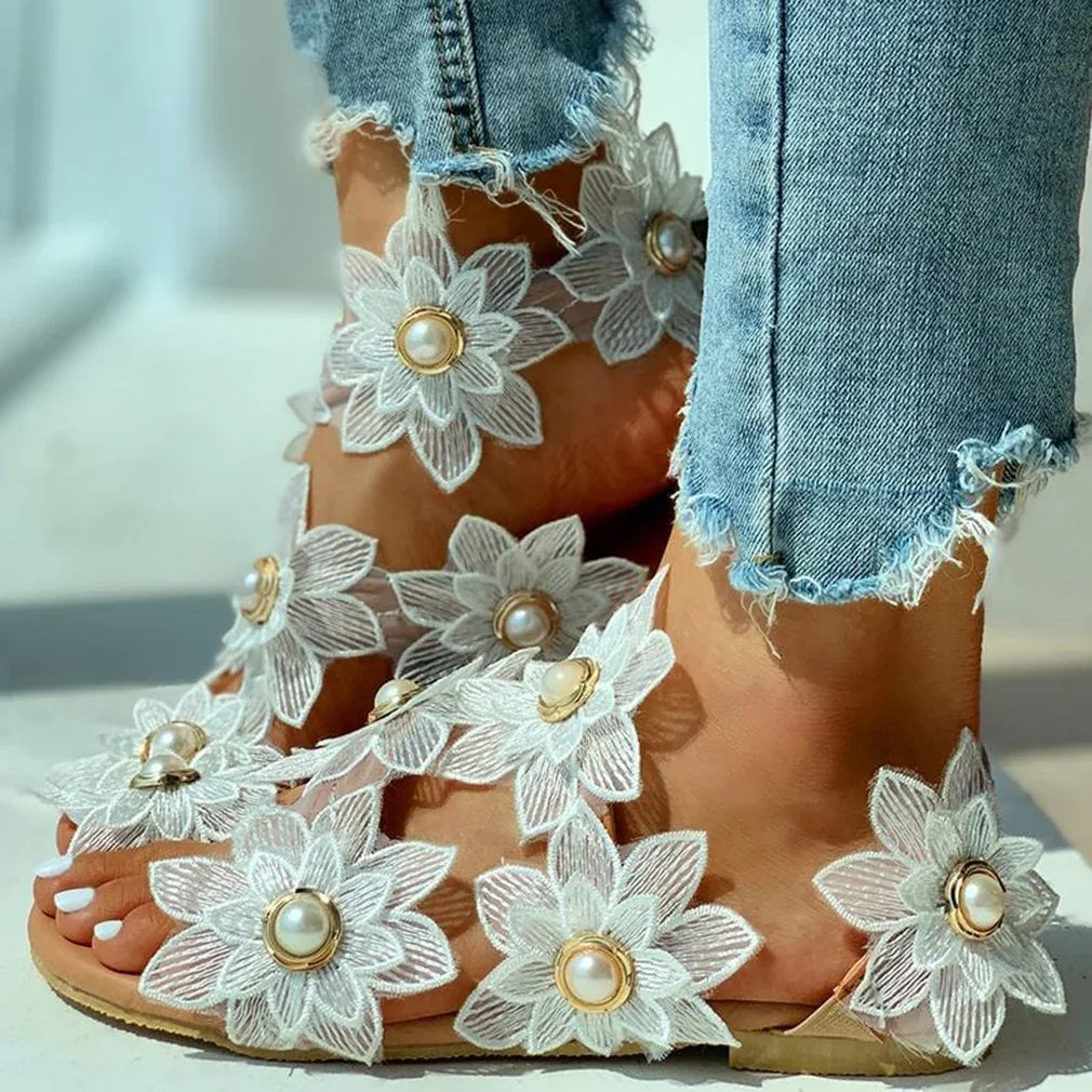 Close-up of feet wearing white floral sandals with pearl accents paired with frayed hem denim jeans
